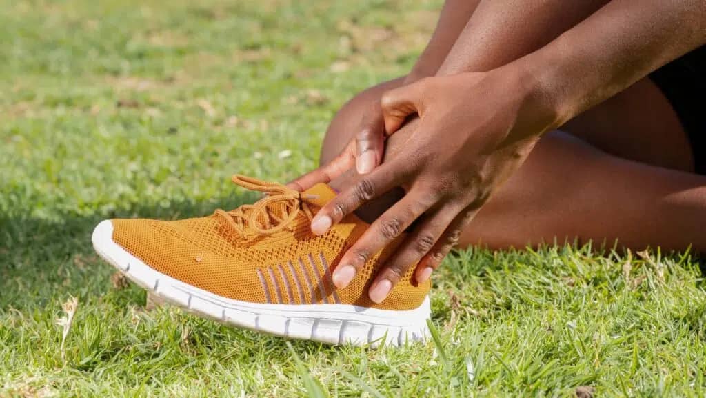 hands on sprained ankle foot in yellow shoes on ground