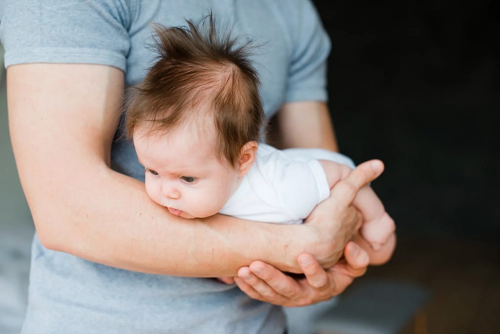 Cute baby laying on hands of father, muscle weakness in babies