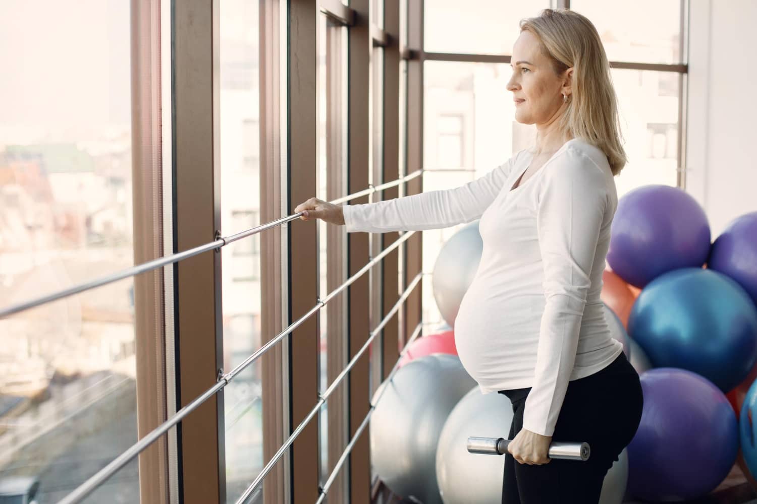 caucasian-pregnant-woman-third-trimester-doing-fitness-excercise-indoors-woman-bright-fitness-studio-with-big-windows-blonde-woman-wearing-whit-shirt-black-leggins