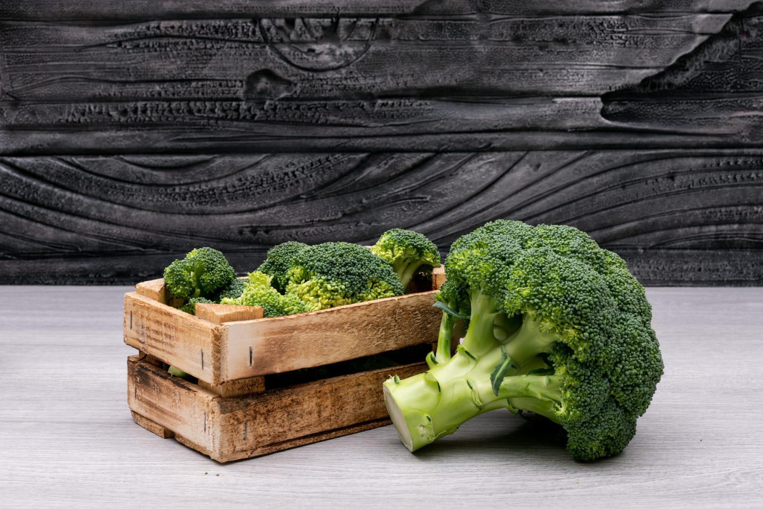 Bunches of broccoli in wooden box near the whole fresh broccoli