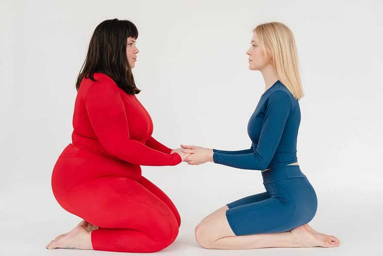 one fat and one slim girl sitting next to each other with hands in hands and keeping eye contact